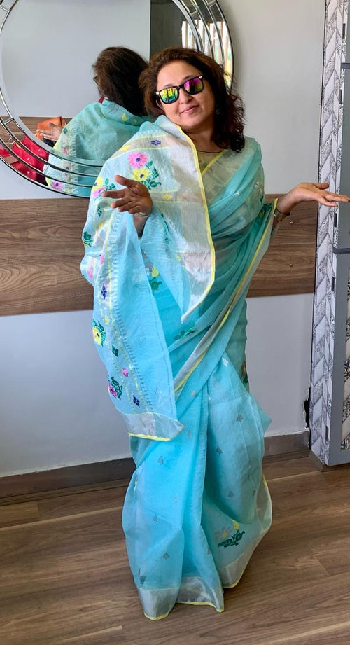 A gorgeous women dressed elegantly in aqua blue real zari kota sari with floral embroidery, wearing sunglasses, posing gracefully in a room with a mirror reflection of her